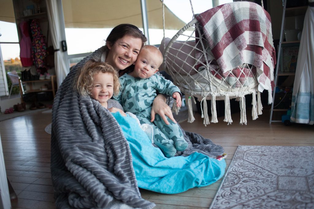 Mama cuddling two children on restful sabbath morning, wrapped in blanket