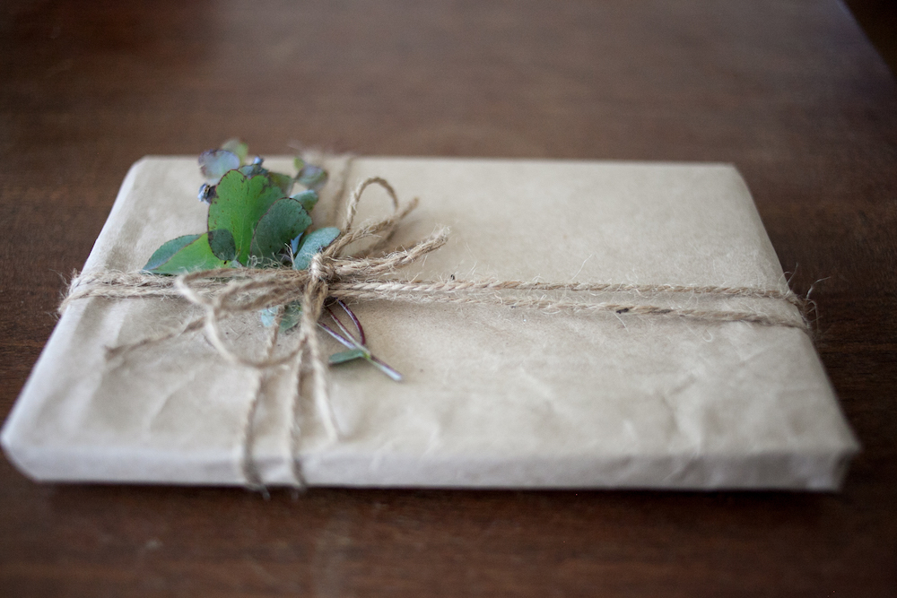small package wrapped in brown paper with brown twine and green leaves