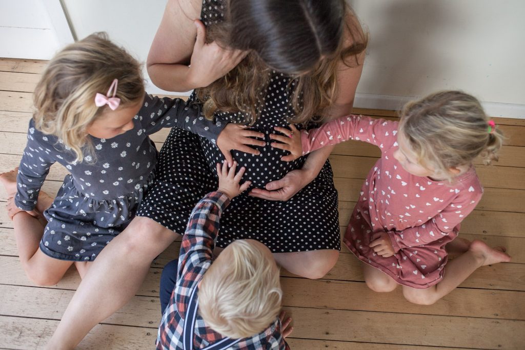 Mama with 3 kids hands on pregnant belly