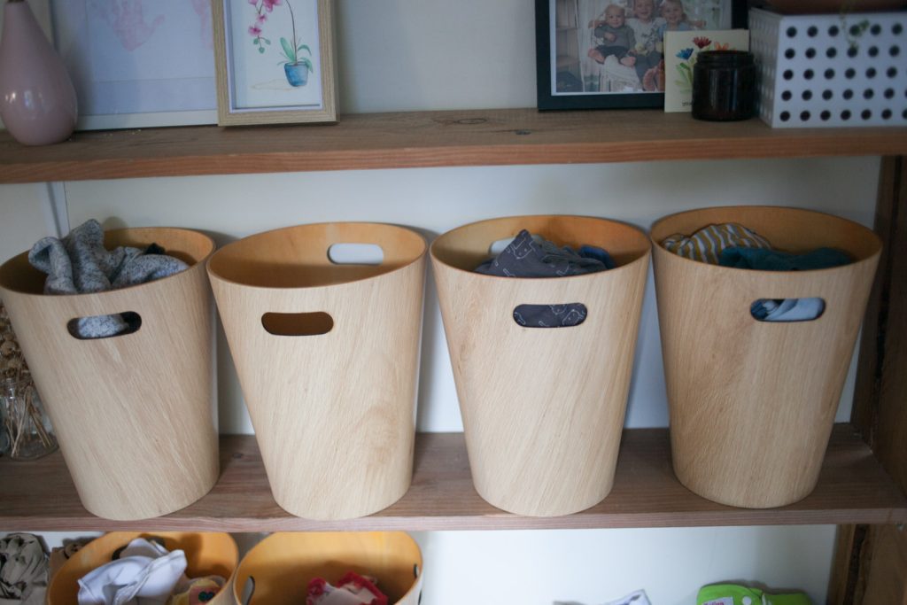 six wastebasket bins for baby's clothing on open shelf