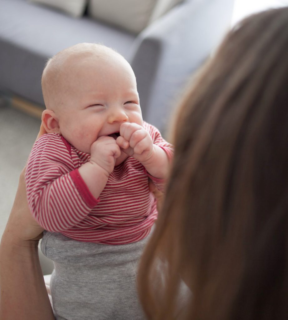 happy baby smiling at mom with hands over mouth