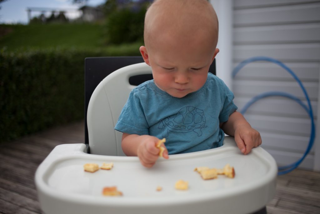 Baby eating sheet pan Swedish pancakes in booster seat with tray