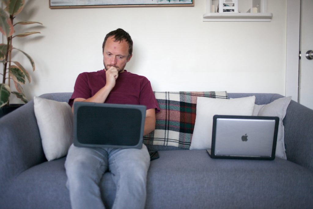 man sitting on couch working on computer during early morning daily summer routine