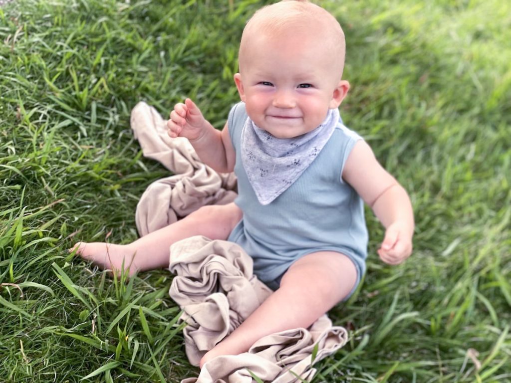 baby sitting on swaddle blanket on grass