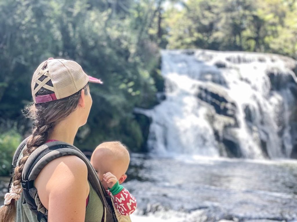 woman looking at waterfall with baby in an ergo baby carrier