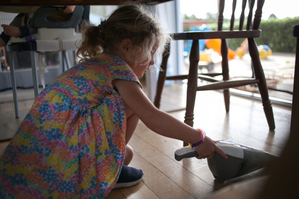 little girl vacuuming under table during dinner clean up time in a daily summer routine
