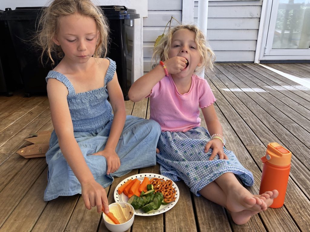 girls snacking on hummus sitting on deck
