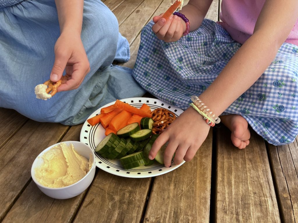 two girls eating veggies dipped in simple hummus