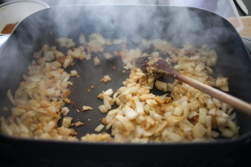 diced onions, garlic, and ginger cooking in electric frying pan with wooden spoon