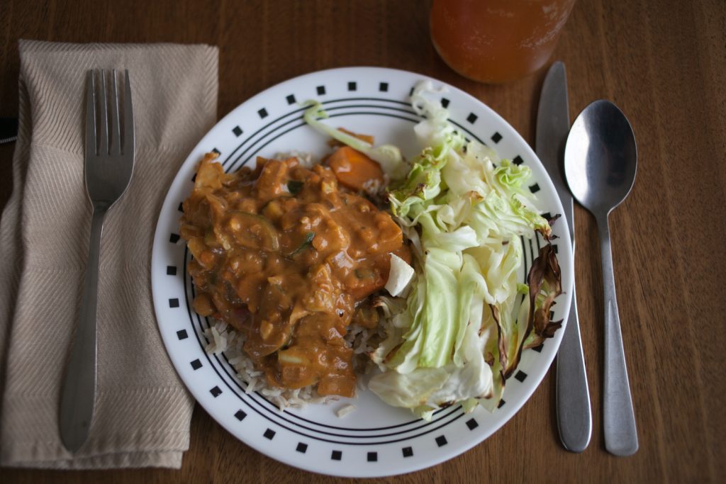 saucy peanut butter curry on rice with roasted cabbage side on white plate with cutlery