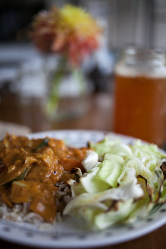 peanut butter curry meal in foreground with flowers and kombucha in background