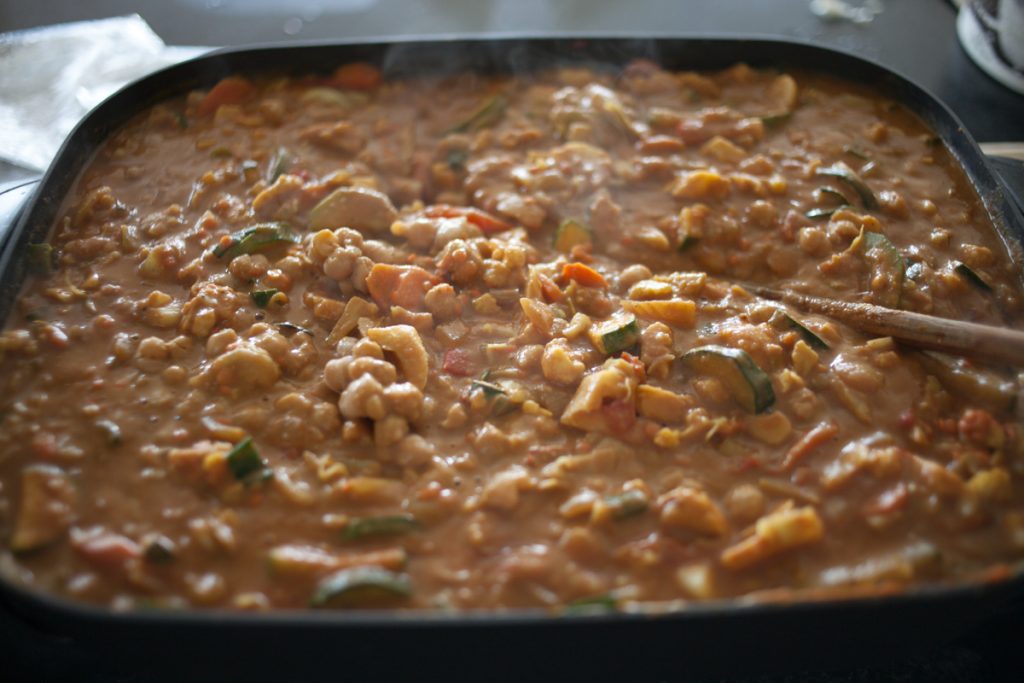 electric frying pan full of chopped veggies, chickpeas, red lentils, chicken, and peanut butter curry sauce