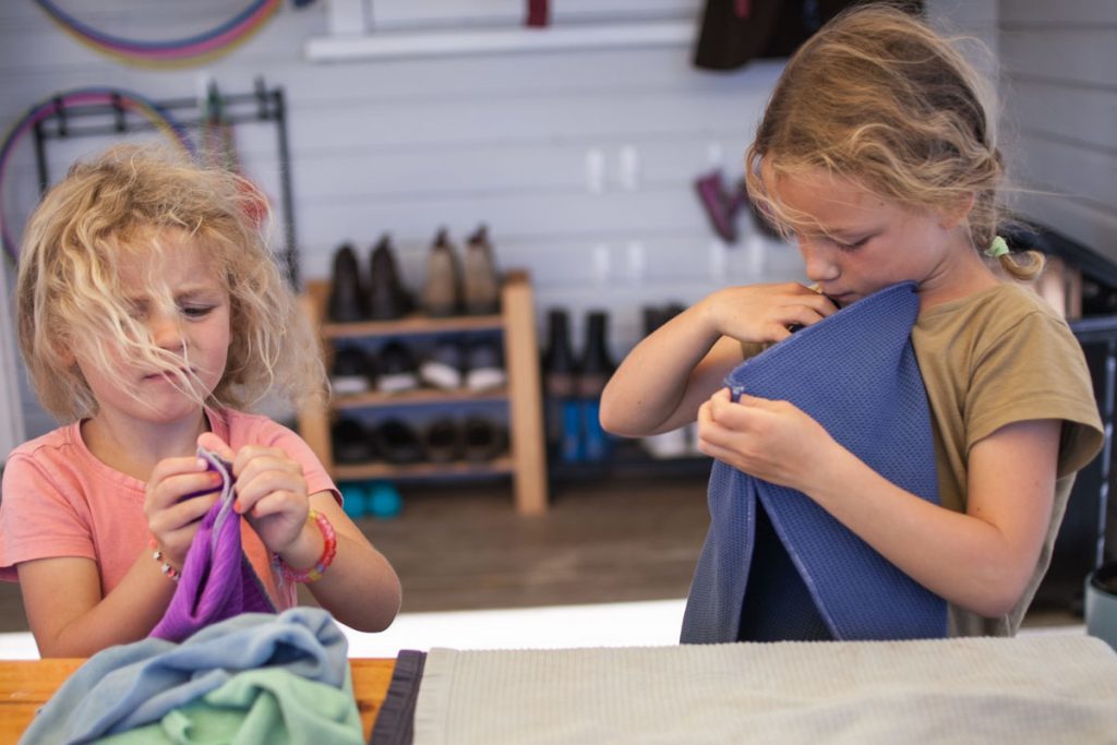 Two girls folding laundry outside on deck for outdoor summer activities with wind blowing their hair