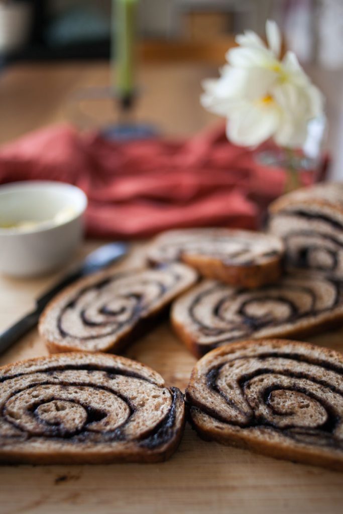 cutting board with pieces of chocolate chai swirl bread on it, butter dish, and flowers in background