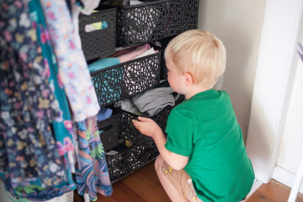 little boy putting away basket of clothes