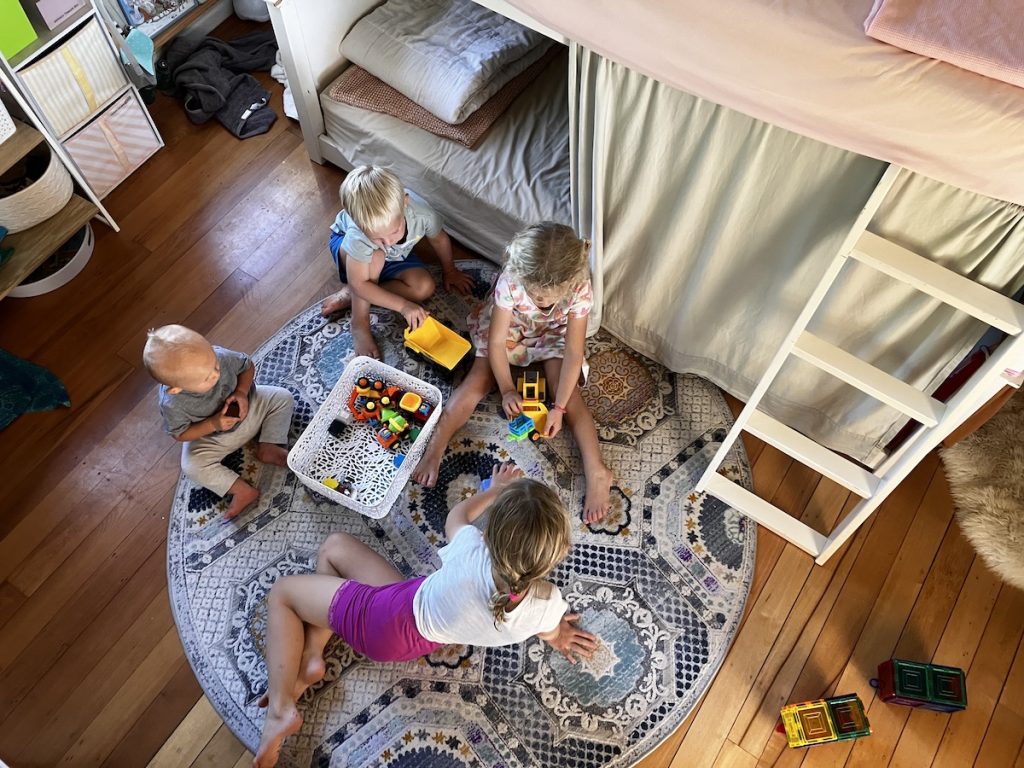 four children playing on rug in shared room with clothes in the shared kids closet to open up floor space for play