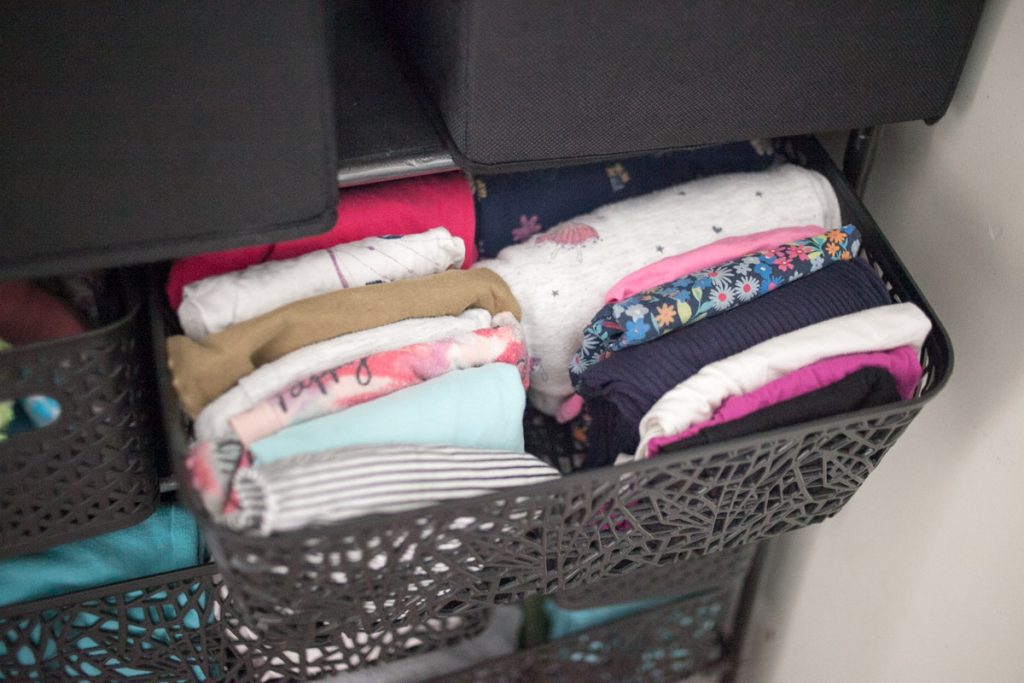 child's shirts and pants in black plastic basket on shoe rack